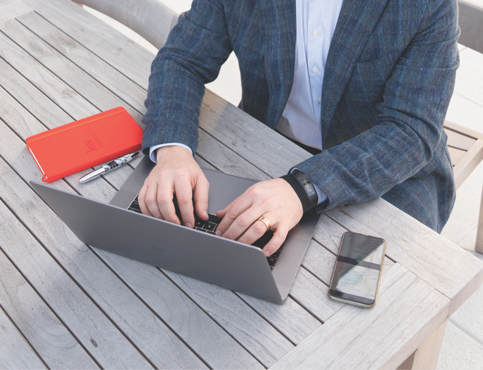 Male using laptop outside with a red KW notebook on the table along with a phone using the KW App.