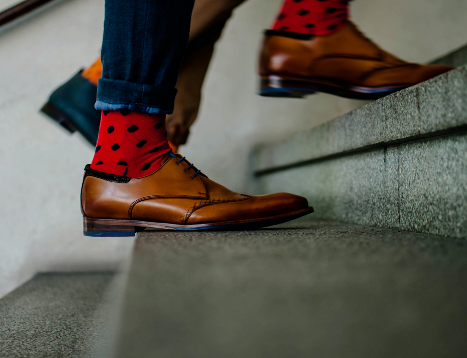 Someone walking up stairs in brown leather shoes with red socks that have black dots visible.