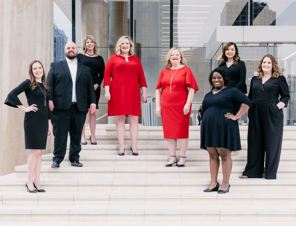 Eight memebers of The Reynolds Team, including Debbie Reynolds and Sarah Reynolds in red, stand on steps together.